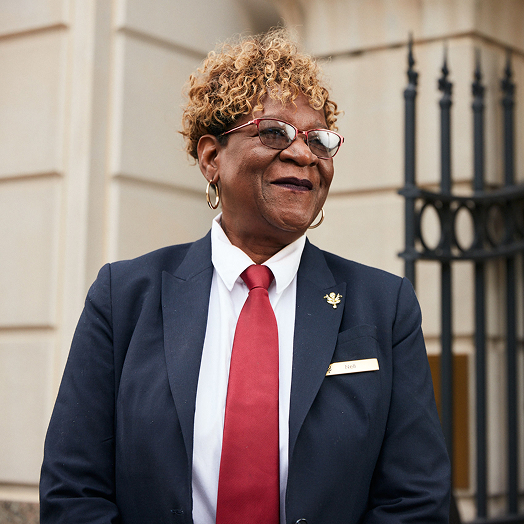 This image depicts a woman smiling in a uniform with a red tie