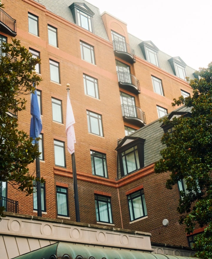Exterior photograph of The Charleston Place hotel showing brick façade and flags.