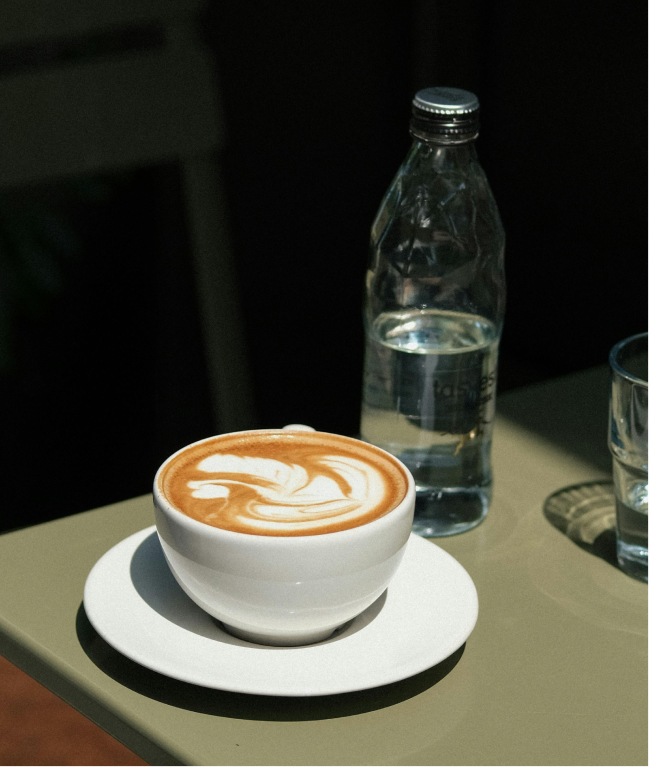 This image depicts a mug with coffee on a table beside a water bottle