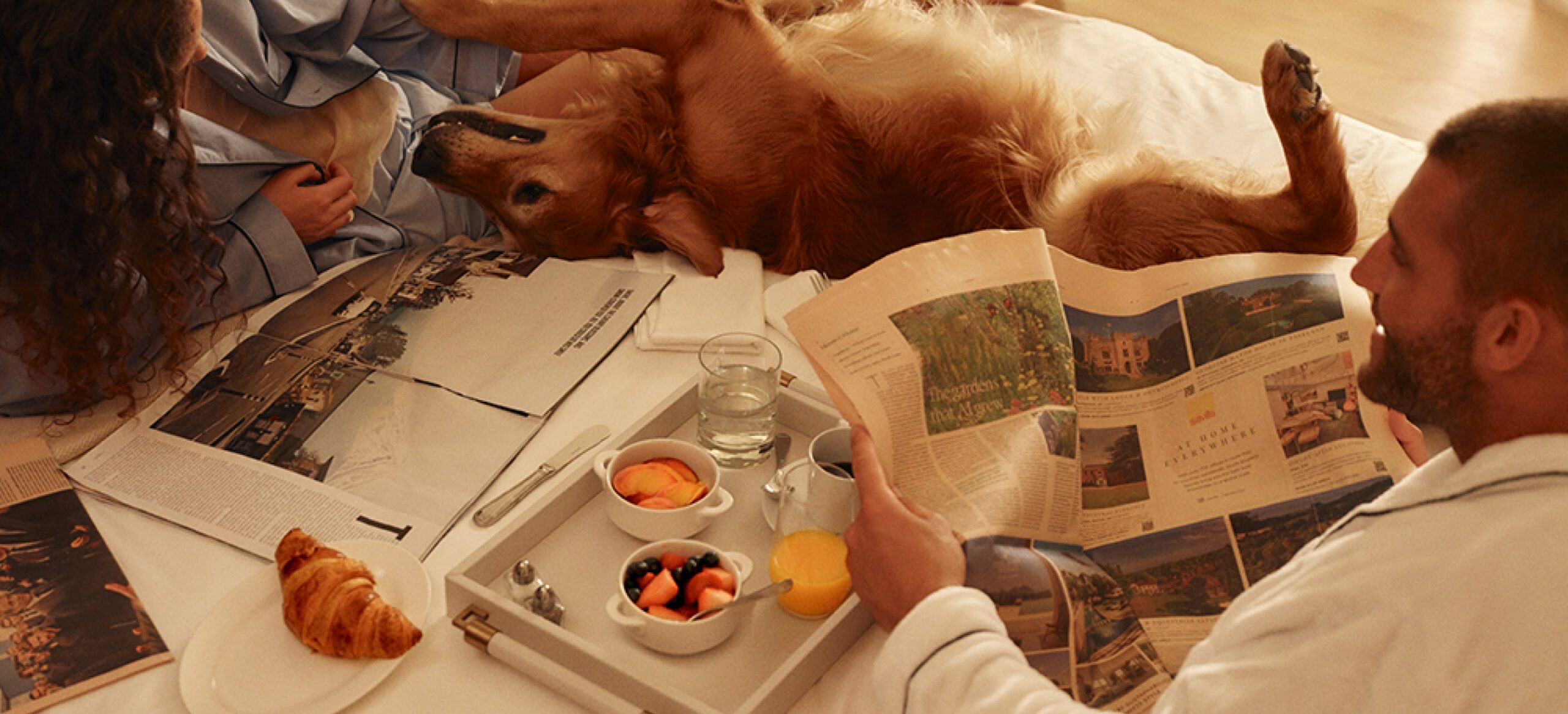 this image depicts a person reading a newspaper in bed with a dog