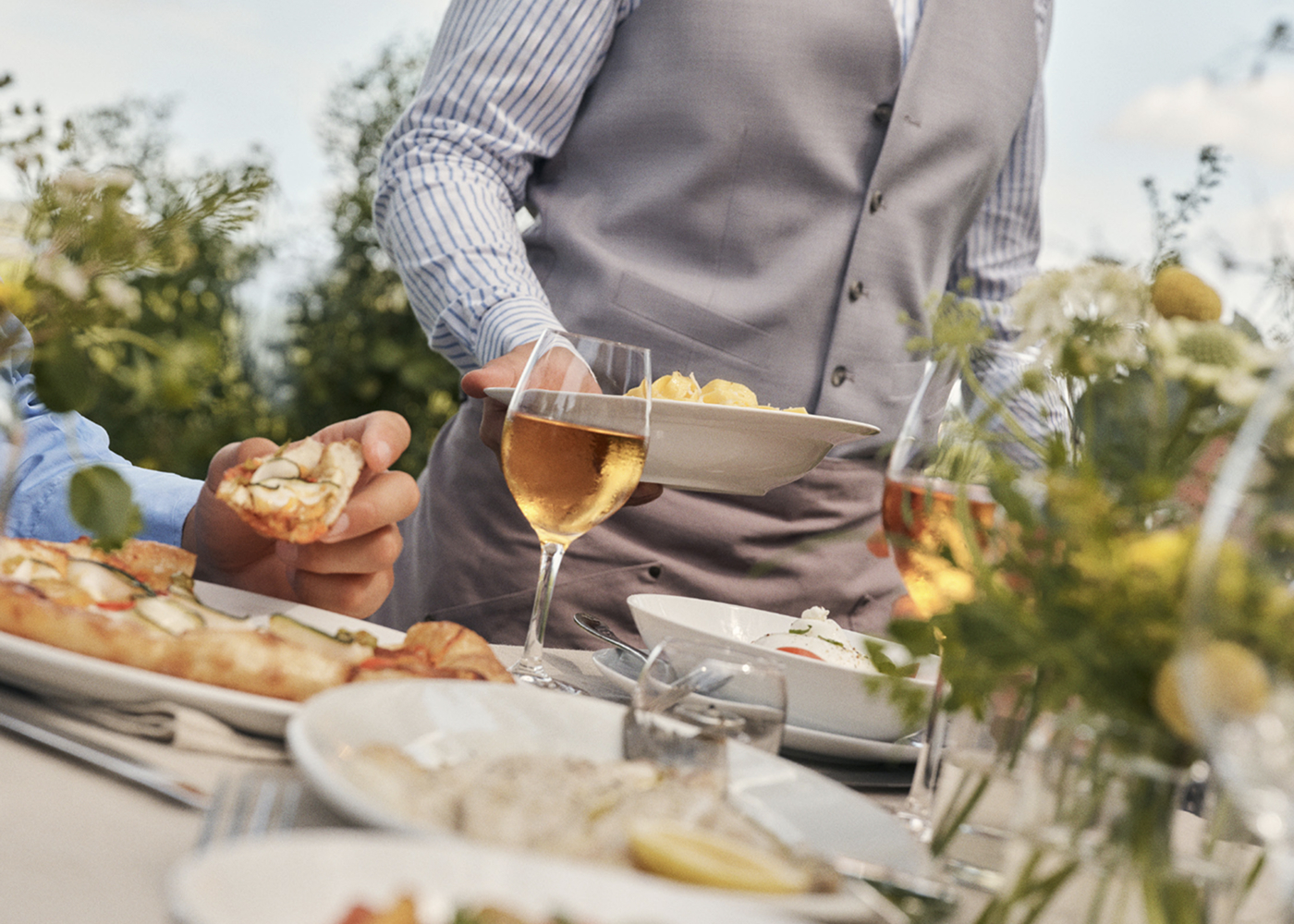 This image depicts a waiter bringing a plate of food to a set table with wine