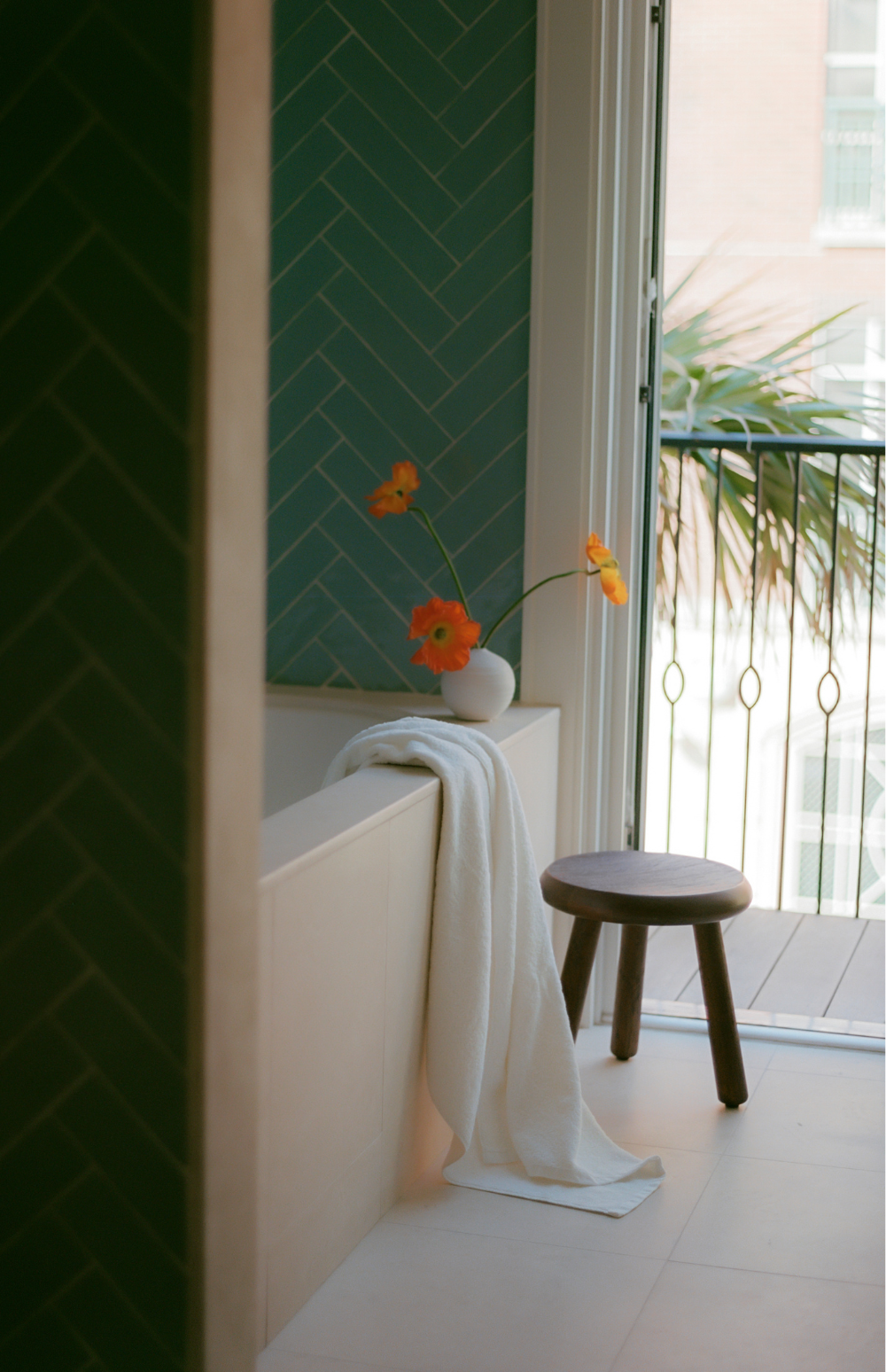 Image of Bathtub and balcony window open and an orange flower