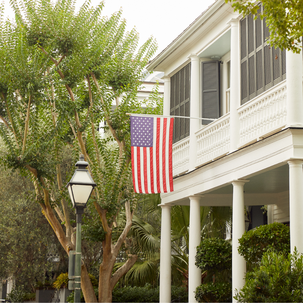 Image of white house with porch and an American flag hanging off the balcony.